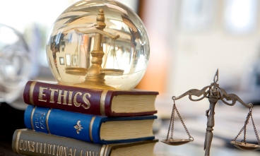 Image of a clear globe with a scale inside it that sits on top of books with the titles Ethics, Civil Code, and Constitutional Law.